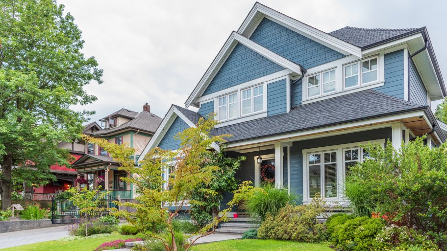 A blue luxury suburban house with gray roof and white trim and green landscaping
